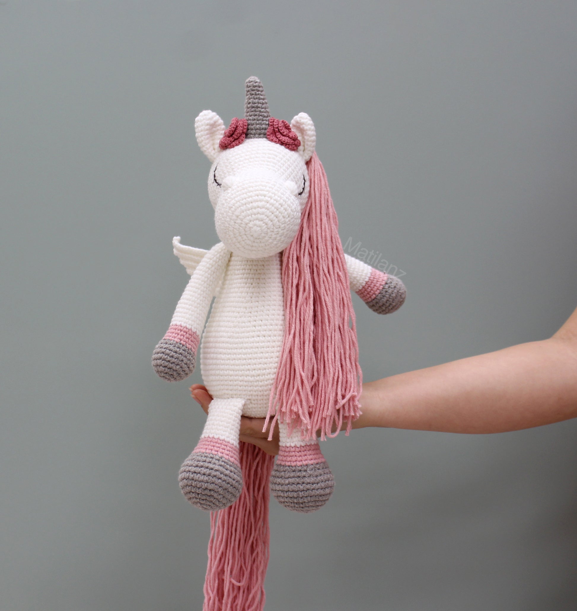 A handmade crochet unicorn with wings, pink mane, and gray horn, 14" tall.