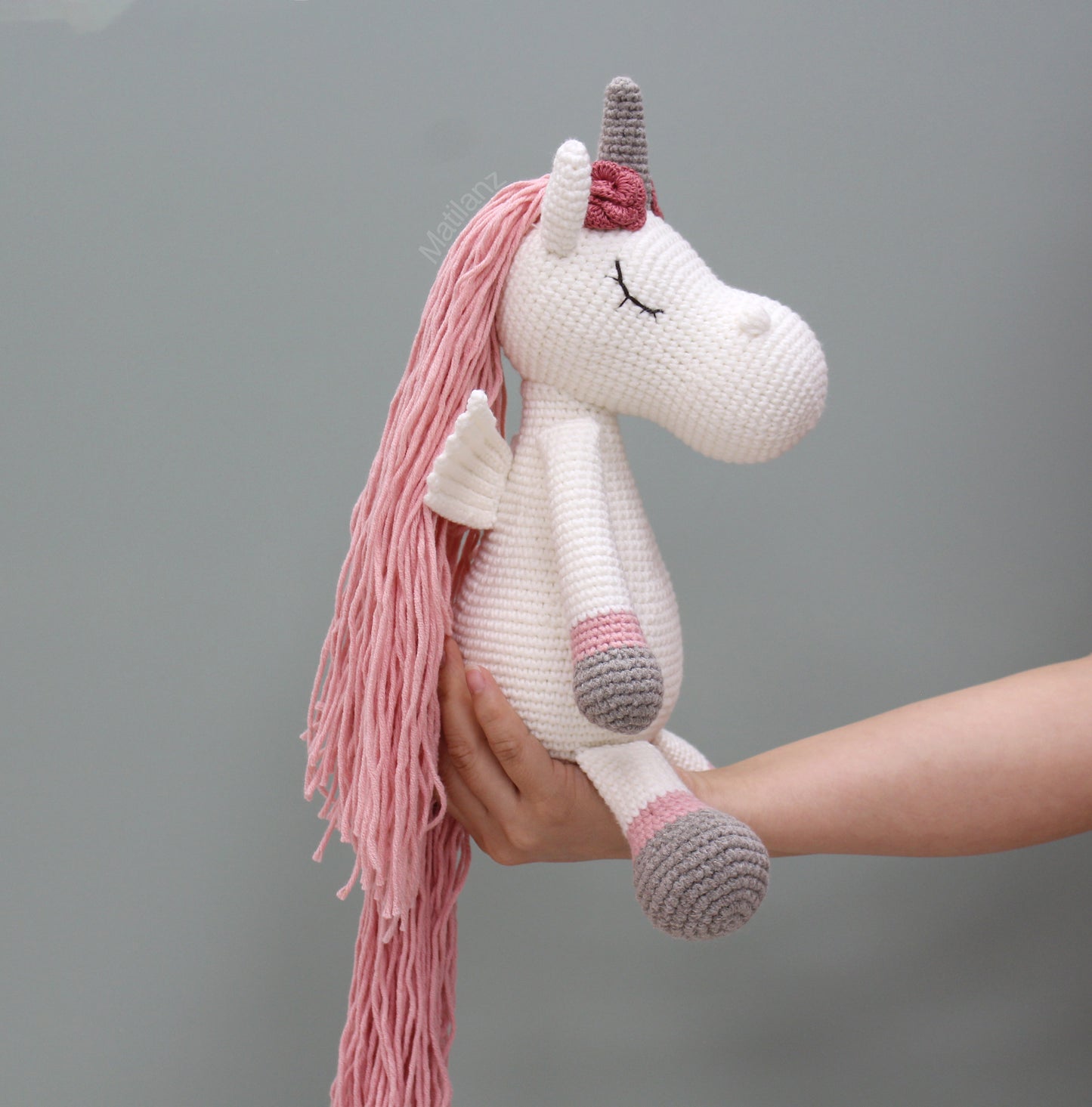 A handmade crochet unicorn with long pink mane, wings, and a gray horn.