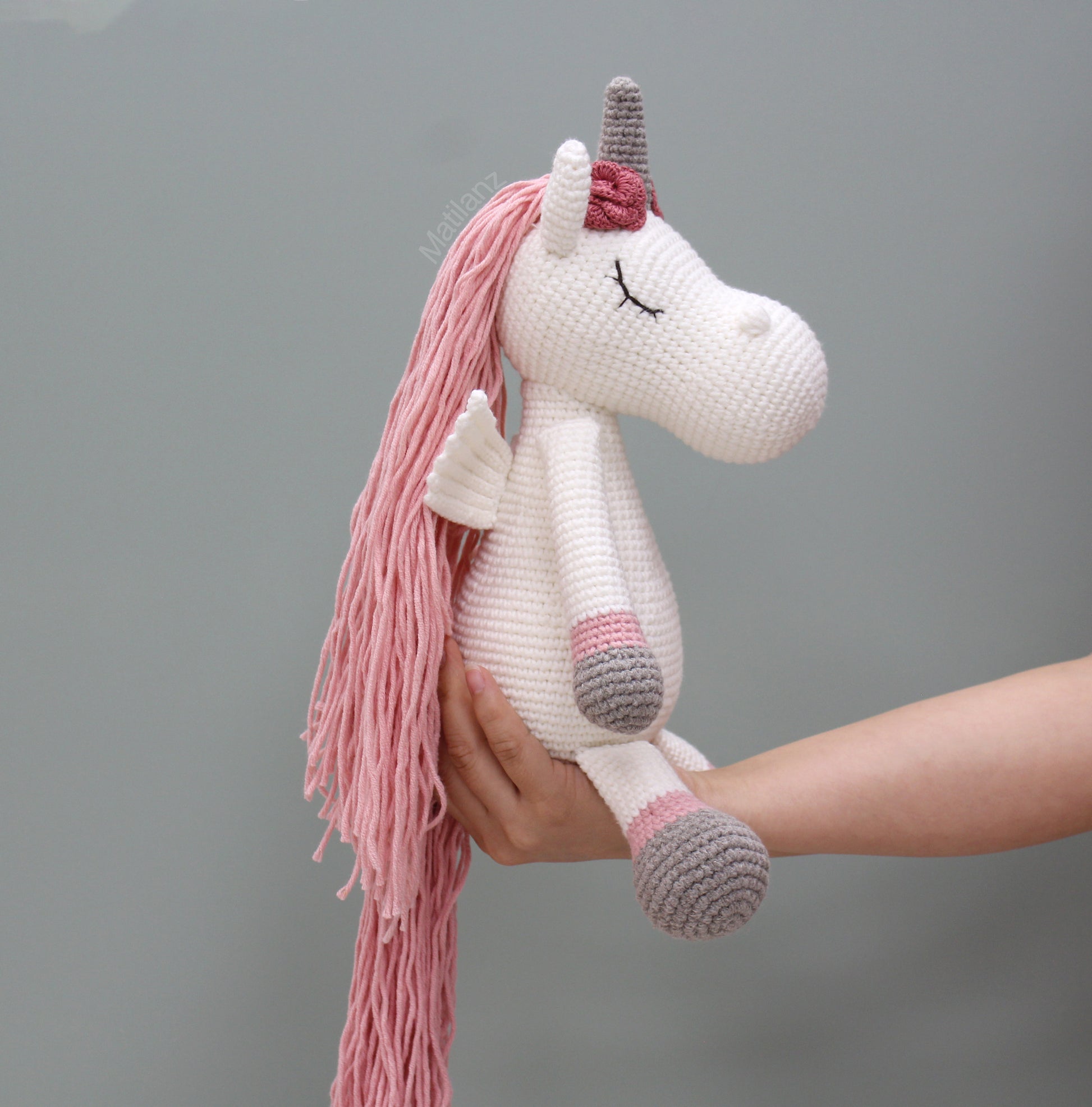 A handmade crochet unicorn with long pink mane, wings, and a gray horn.