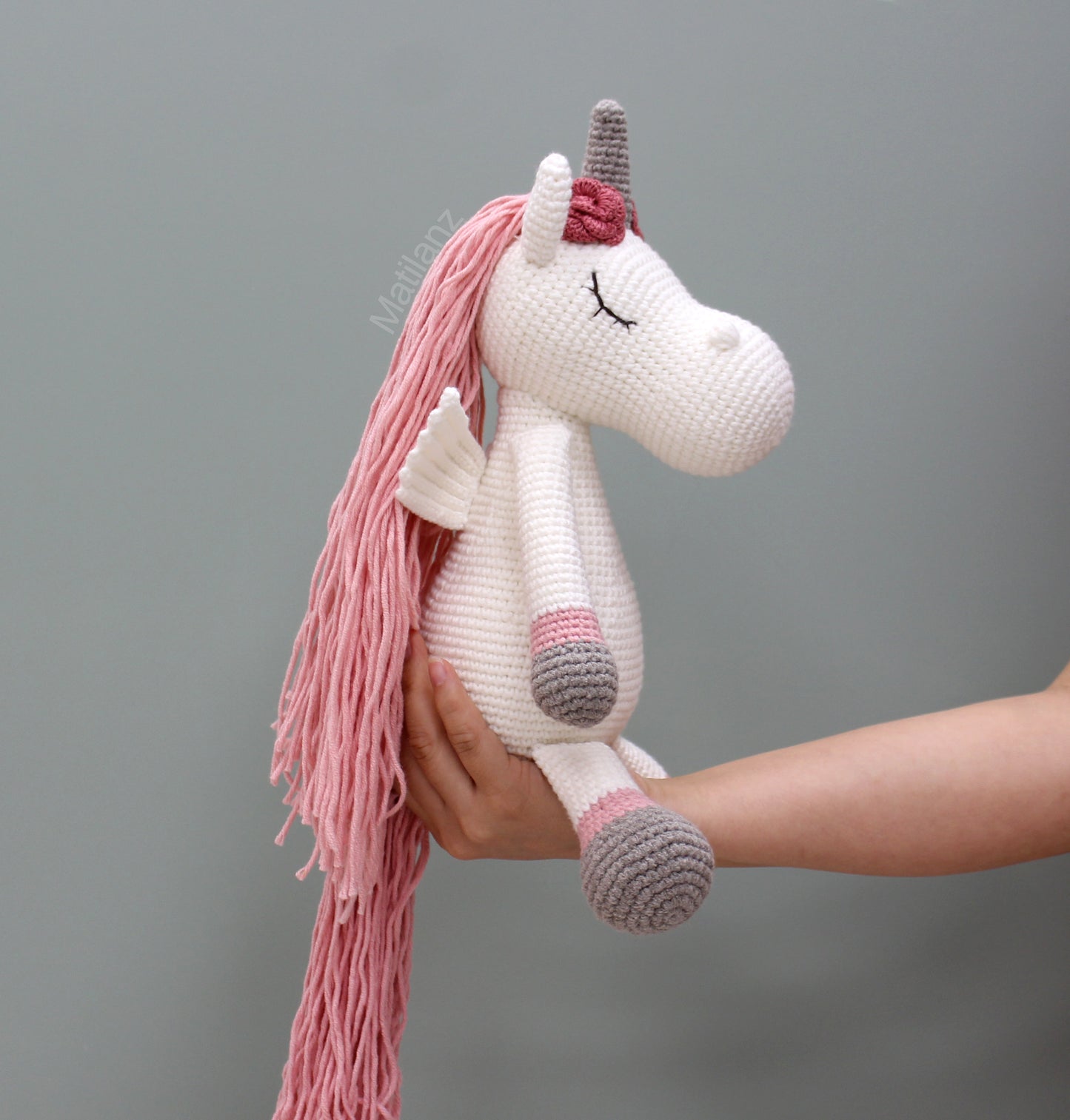 A handmade crochet unicorn with a long pink mane, wings, and a gray horn.