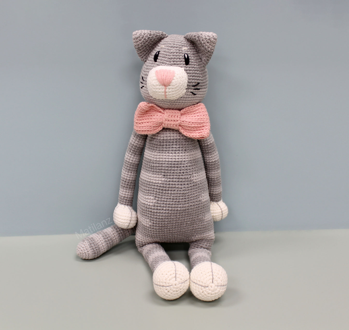 Gray crochet cat plush with pink bow tie and white paws, 18 inches tall.