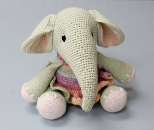 Crochet plush elephant in soft green with pink ears, holding a colorful blanket.