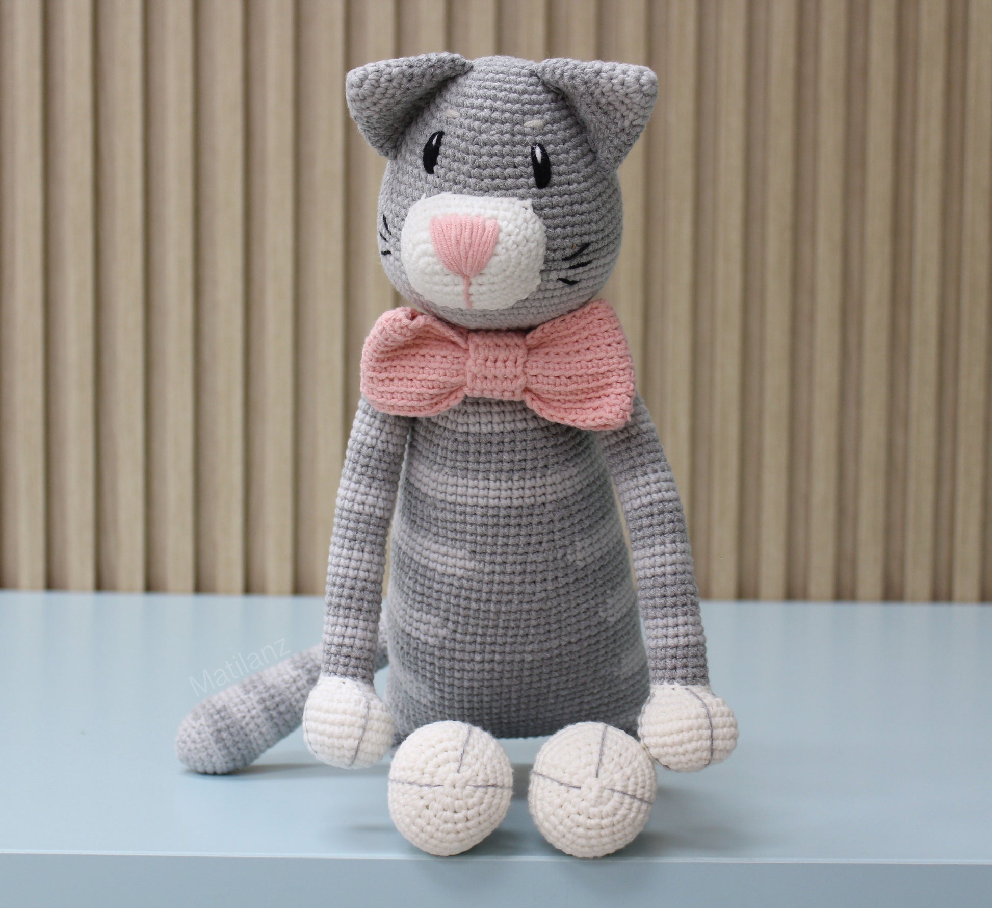 "Large gray crochet cat plush with a pink bow, handmade and cute."