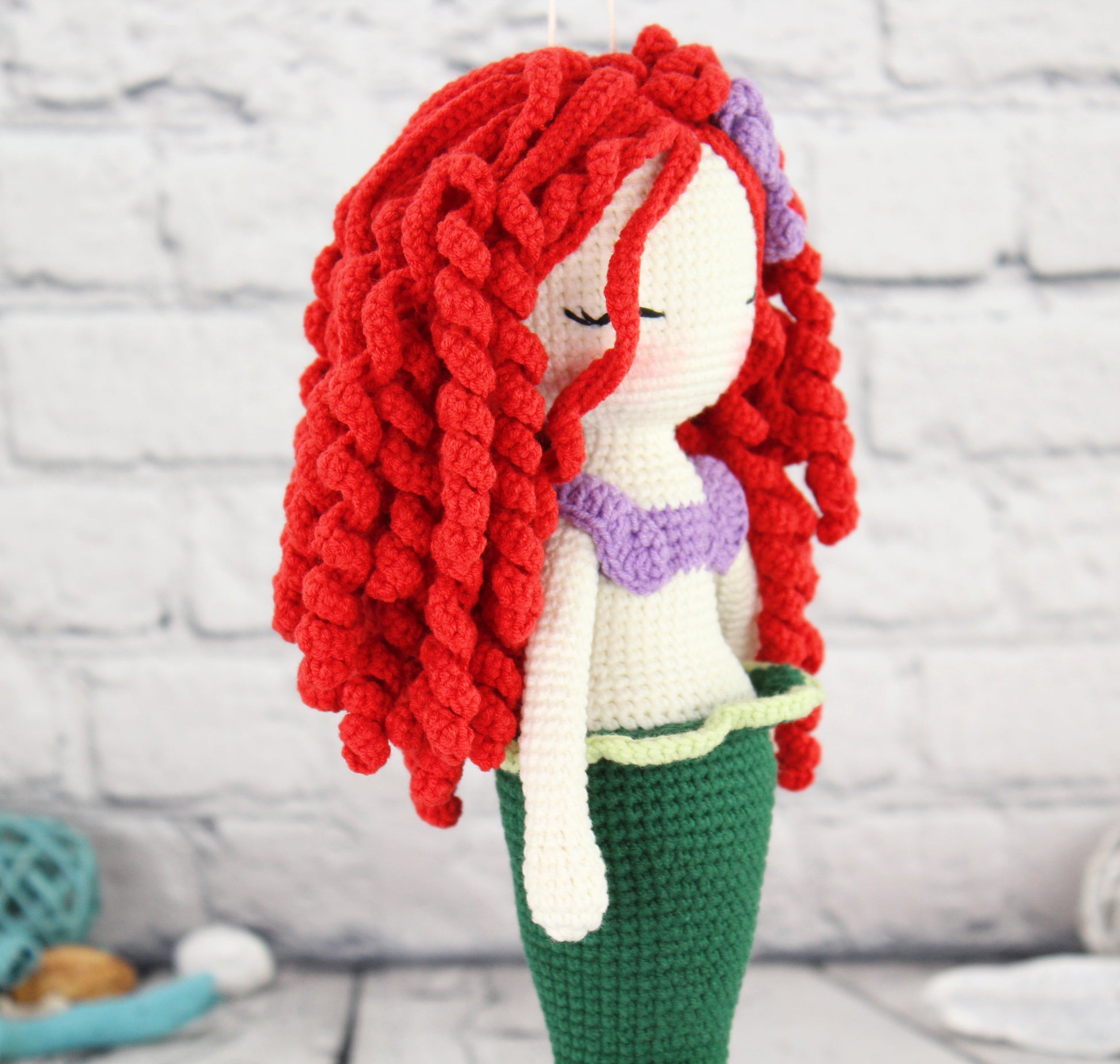 A handmade crochet mermaid doll with long red hair, purple top, green tail, and a white beard.