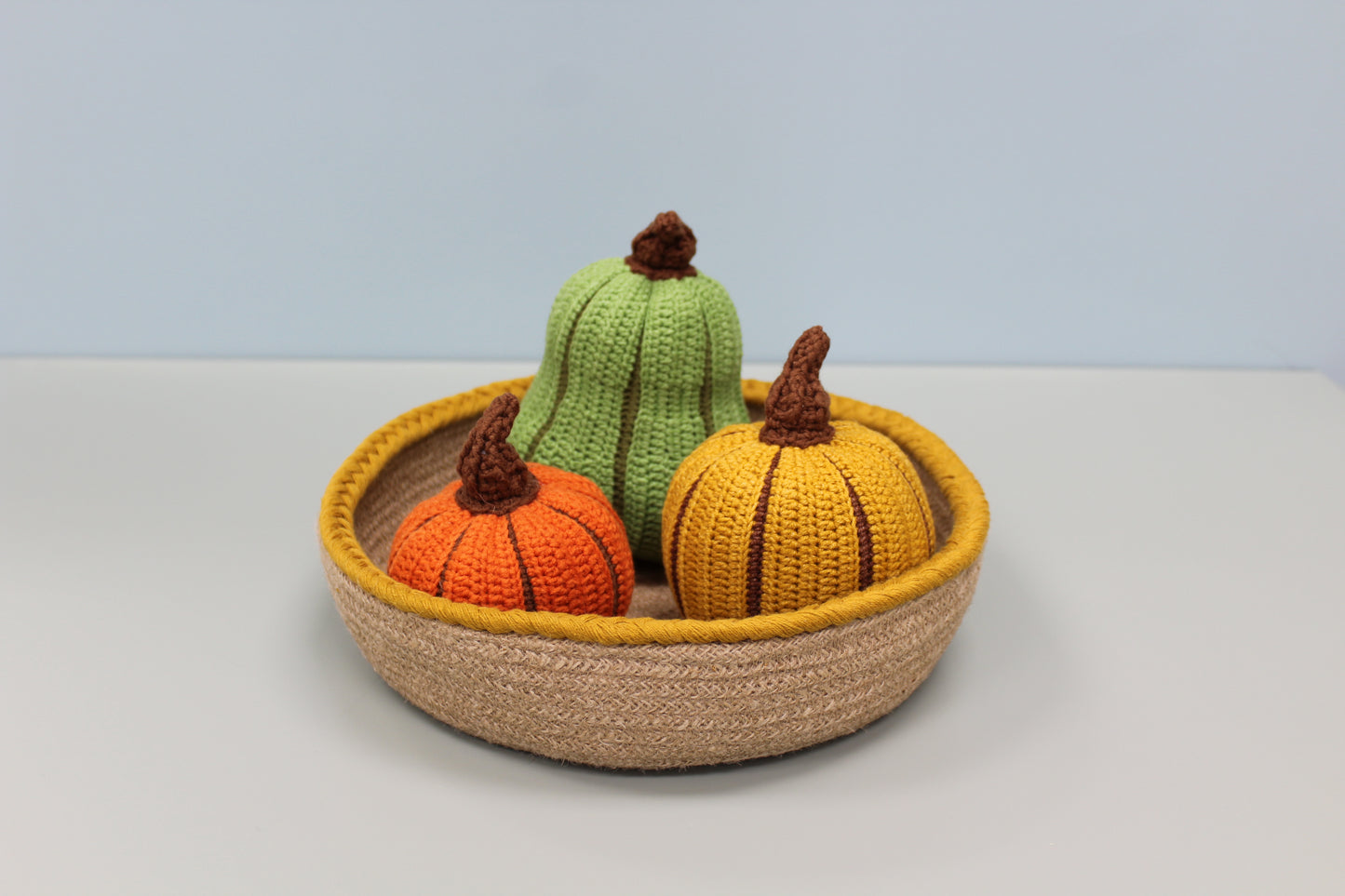 Knitted pumpkins in a woven basket on a light background