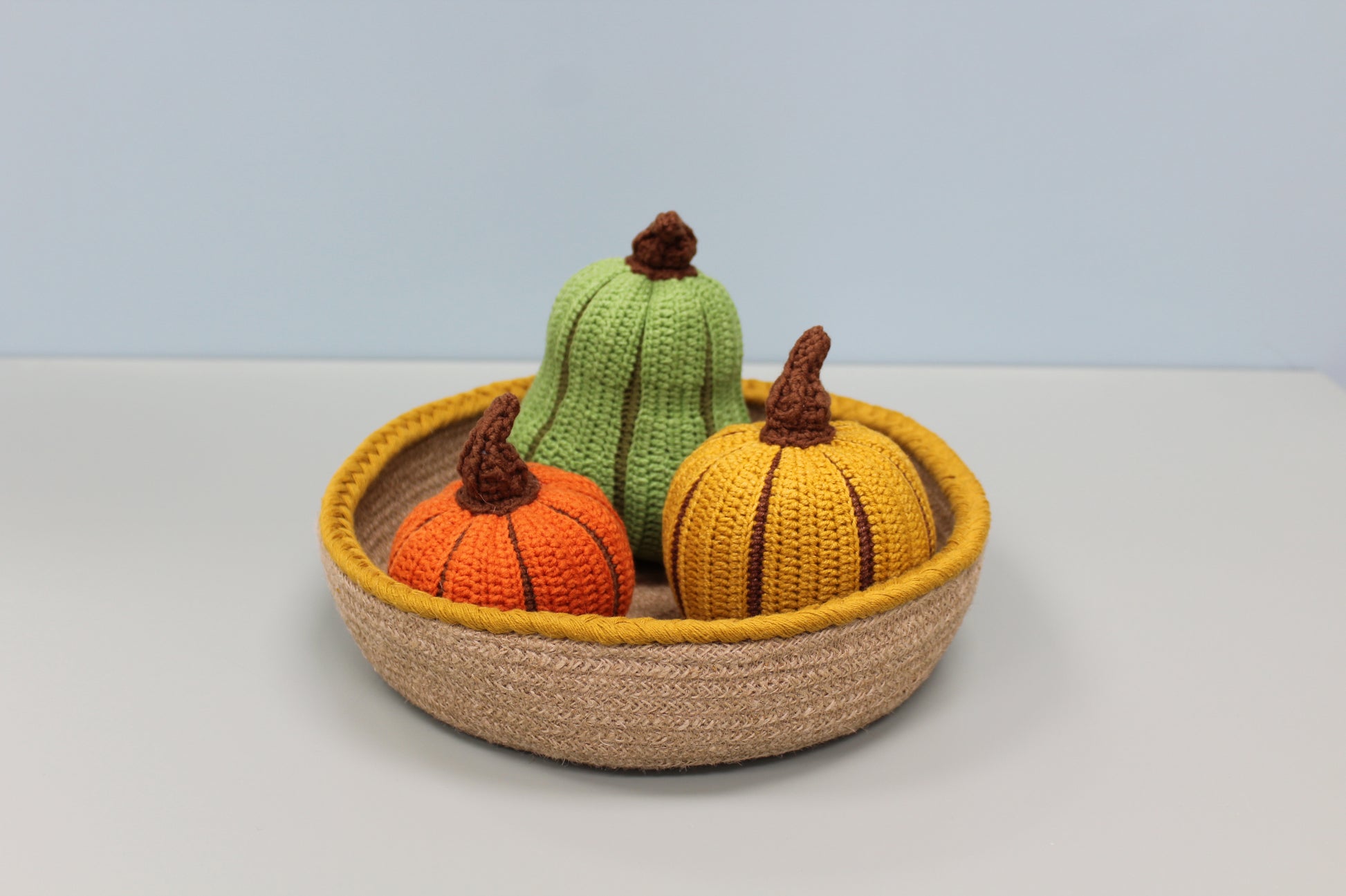 Knitted pumpkins in a woven basket on a light background