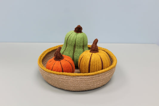 Knitted pumpkins in a woven basket on a light background
