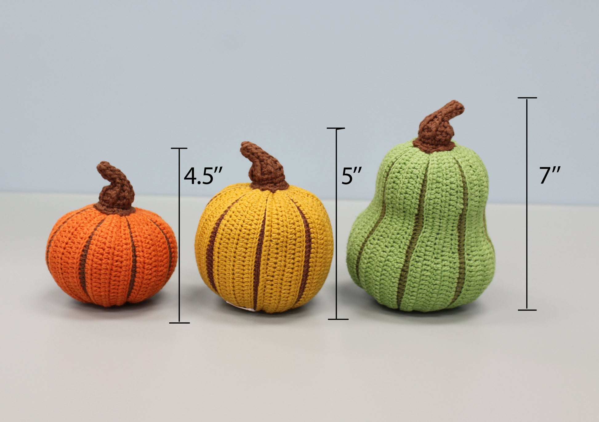 Three crocheted pumpkins in orange, yellow, and green with measurements on a light gray background