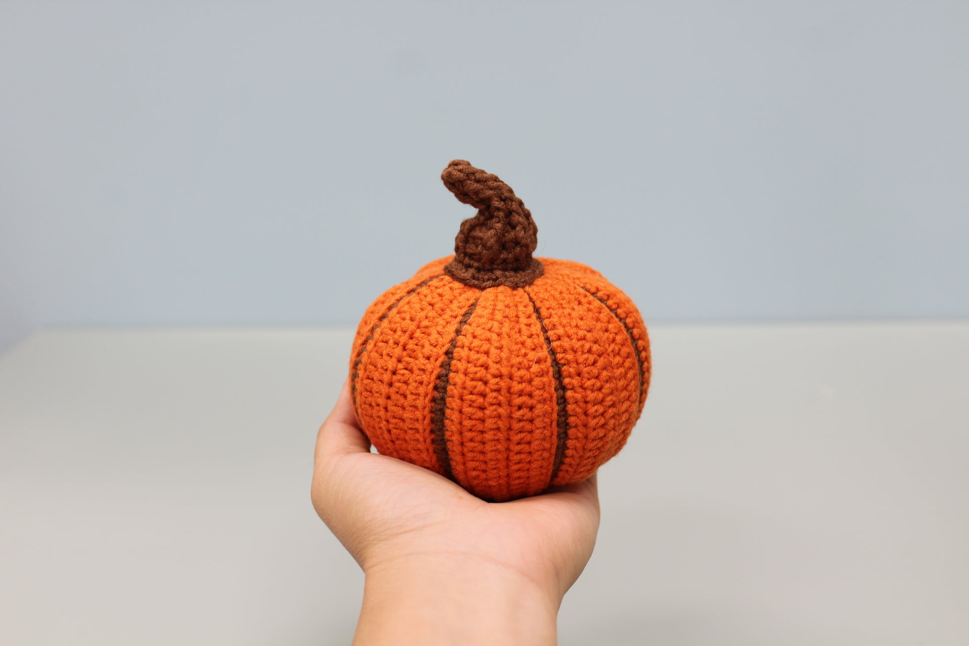 Hand holding a small crochet pumpkin against a plain background