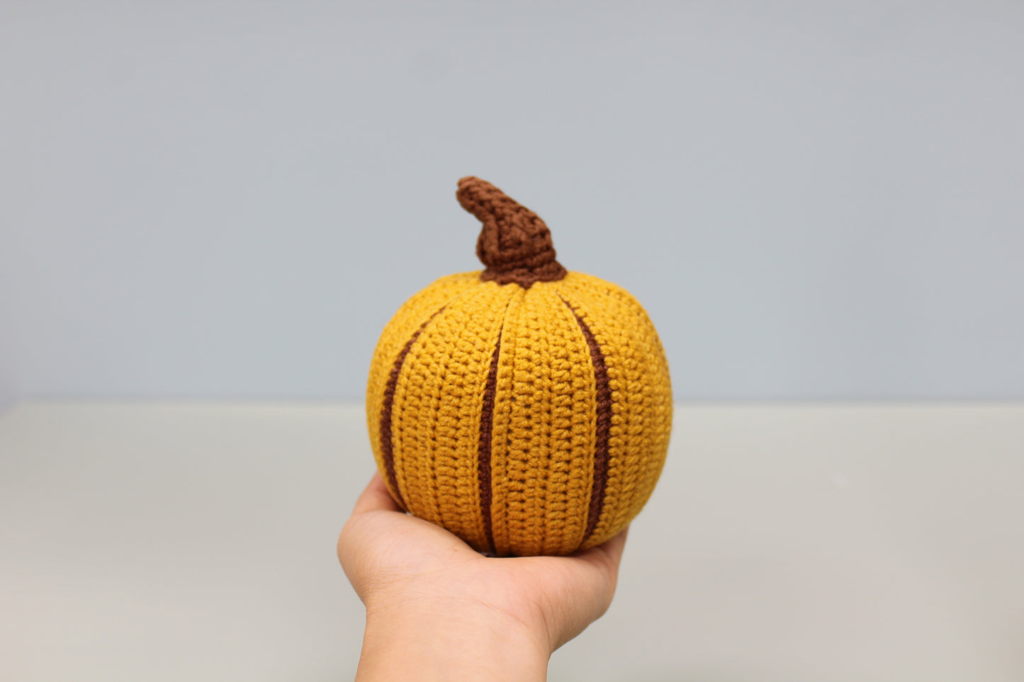 Hand holding a knitted pumpkin against a plain background