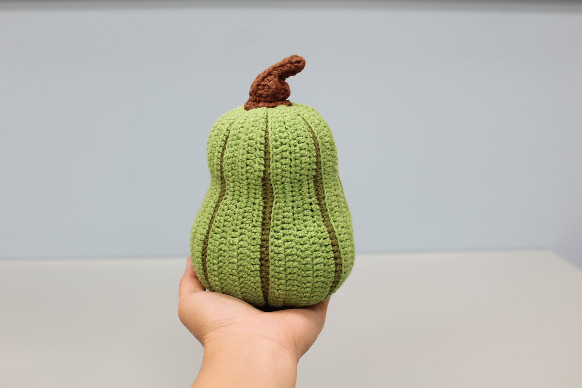 Hand holding a green knitted pear against a plain background