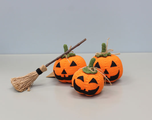 Handmade crochet plush orange pumpkin with a green stem and black jack-o'-lantern face.