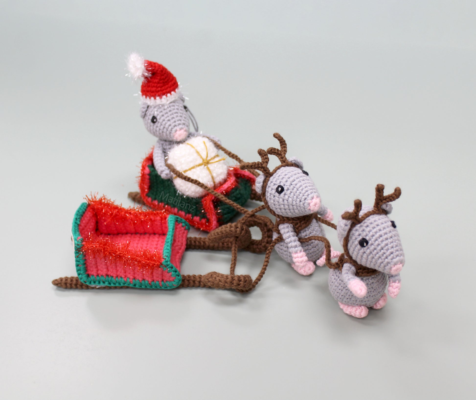 "Handmade crochet Christmas mice with antlers pulling a red and green sleigh, decorated with a Santa hat and festive details."