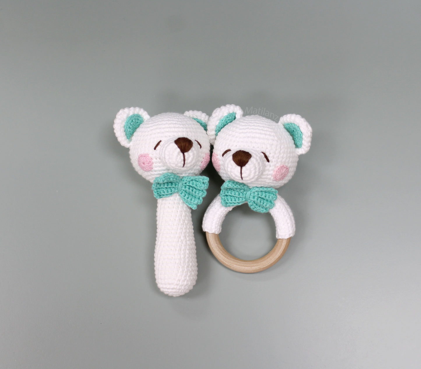 Two handmade crochet bear rattles with white fur, teal bows, and wooden rings, crafted from 100% cotton.