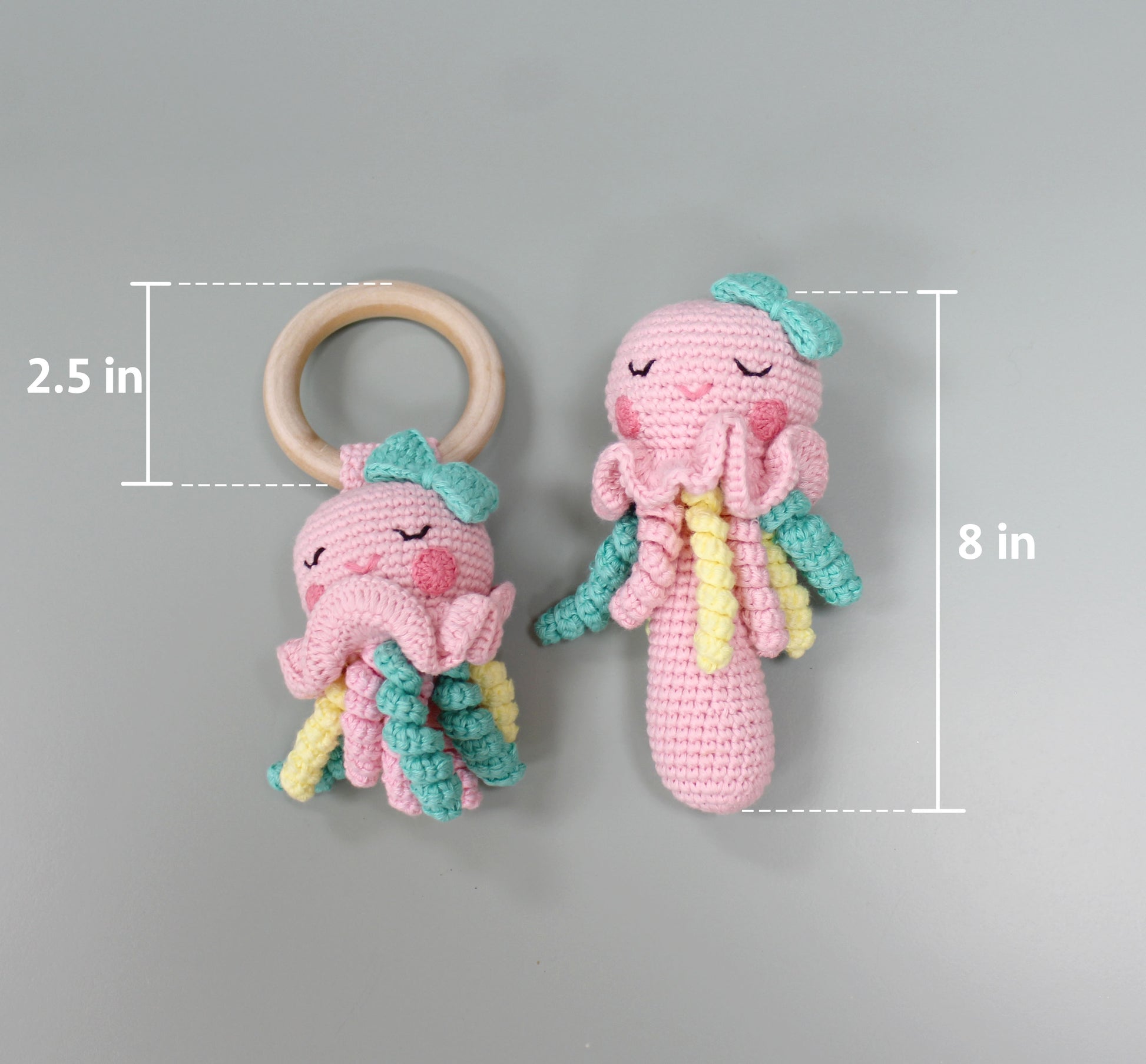 Handmade pink crochet jellyfish rattle with teal and yellow tentacles, 8 inches tall, paired with a 2.5-inch wooden ring.