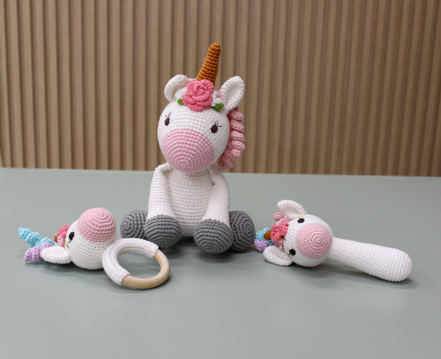 "Handmade crochet unicorn baby toy set features a white unicorn with pink accents, teether, rattle, and ring for sensory play."