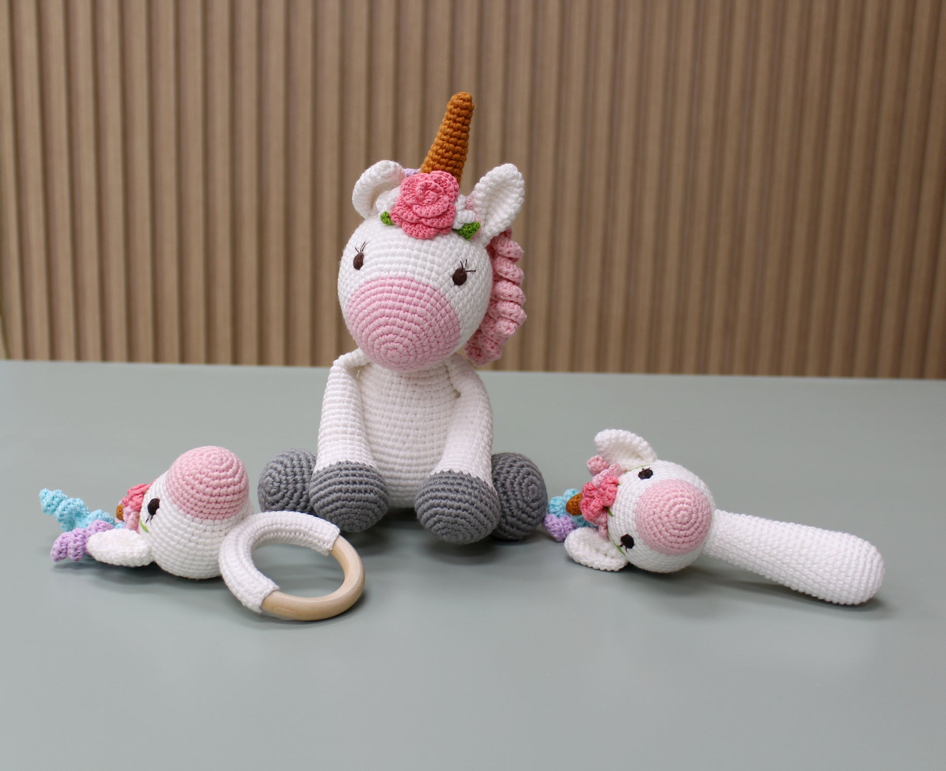 "Handmade crochet unicorn baby toy set features a white unicorn with pink accents, teether, rattle, and ring for sensory play."