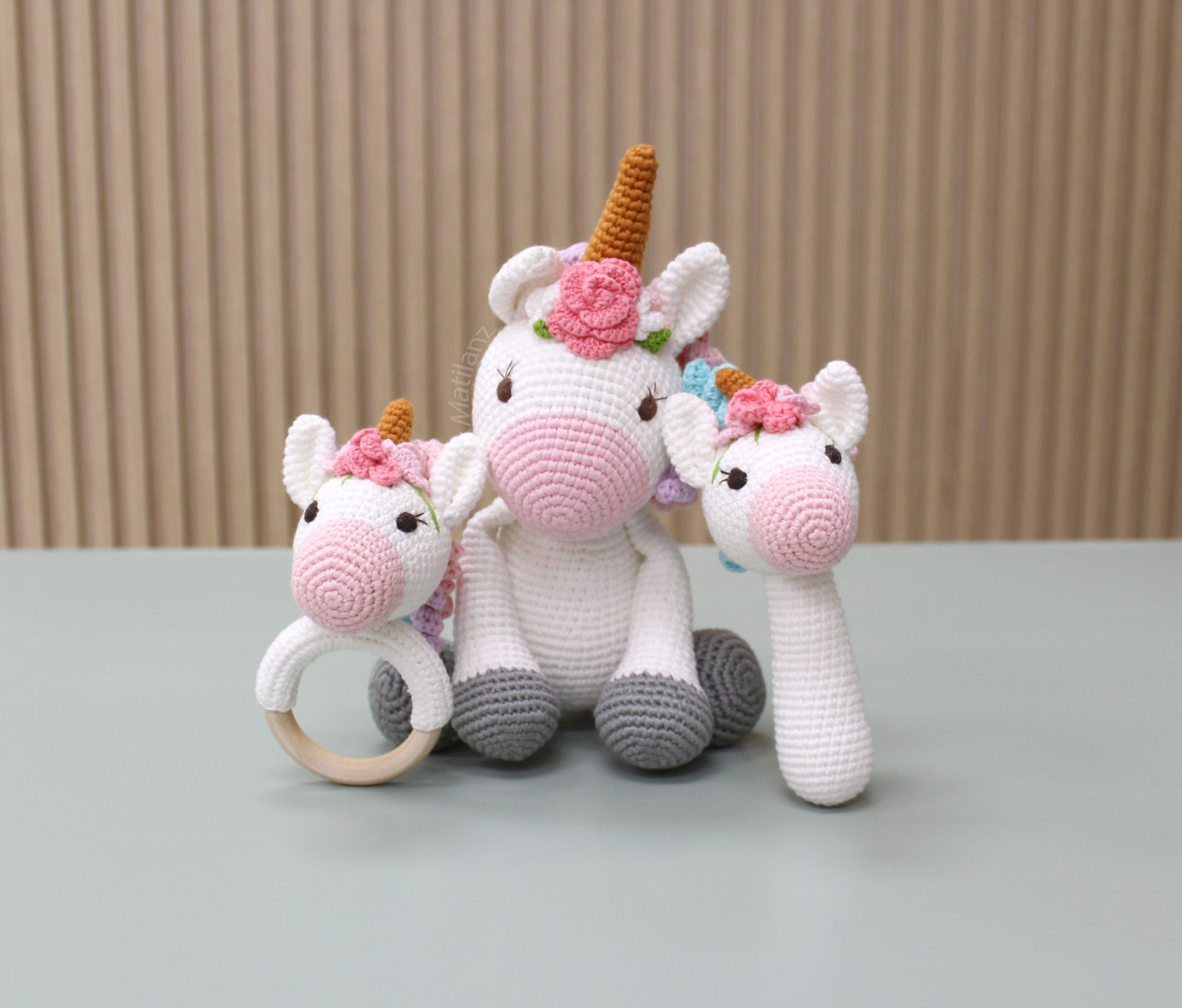 "Handmade crochet unicorn-themed baby toy set, featuring a baby rattle, teether, and soft plush toy with floral accents."