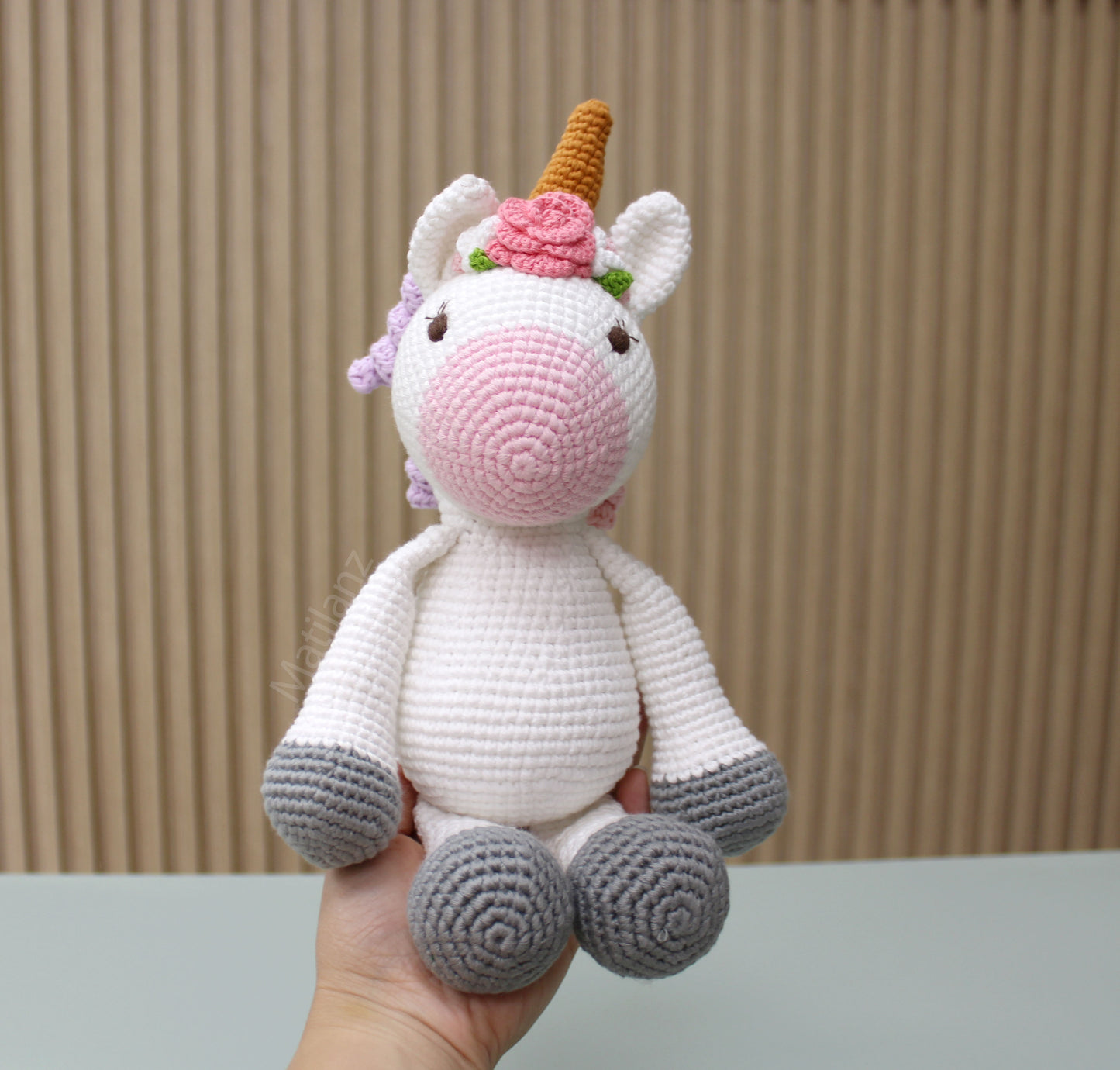 "Adorable handmade crochet unicorn toy with pink and white body, gray accents, golden horn, and floral crown."