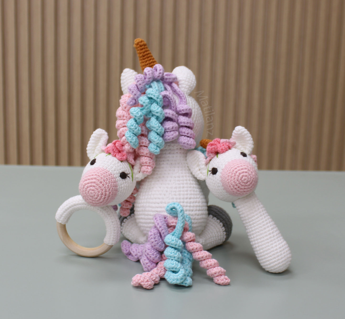 Handmade crocheted unicorn toy set in pastel colors with textured yarn details and a wooden ring.