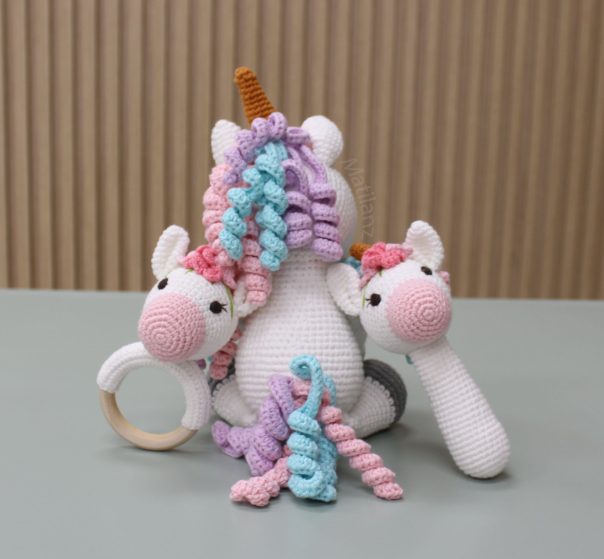 Handmade crocheted unicorn toy set in pastel colors with textured yarn details and a wooden ring.