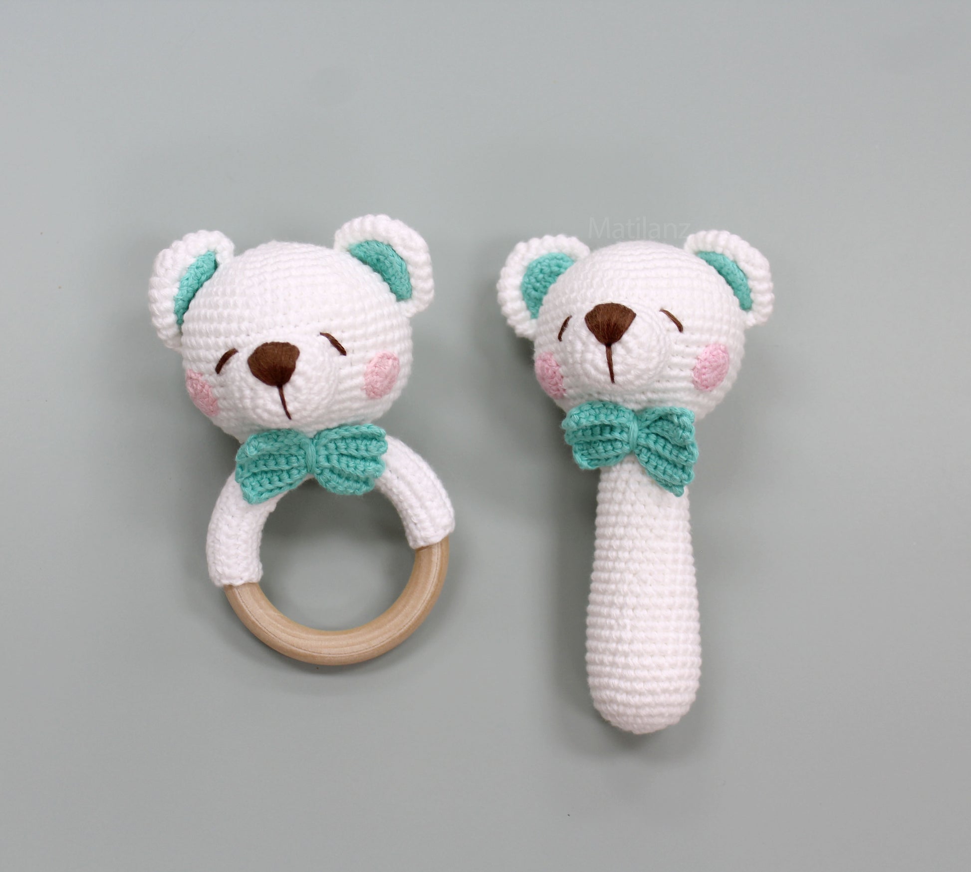 Handmade white crochet bear rattle toy with green bow tie and wooden ring, soft and playful for babies.