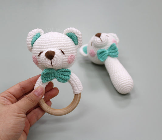 Handmade crochet bear rattle toy in white with teal accents, featuring a wooden ring and bow tie.