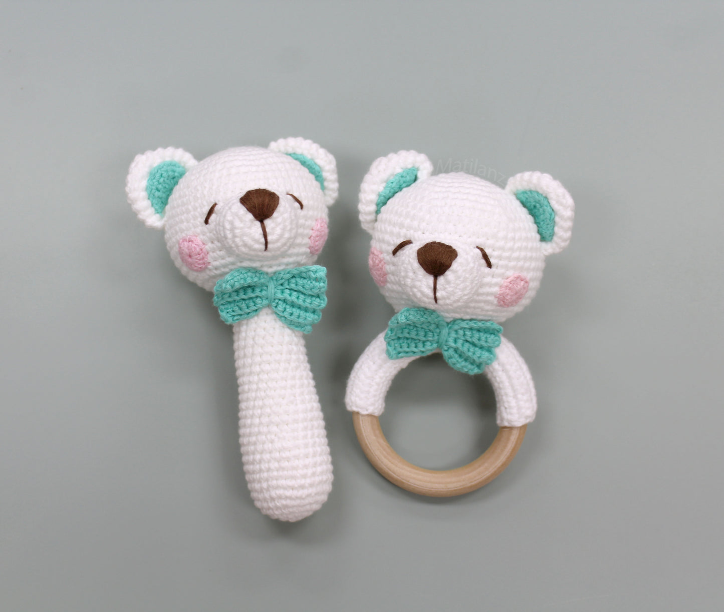 A handmade crochet bear rattle and teether set in white with teal accents and a wooden ring, ideal for sensory play.