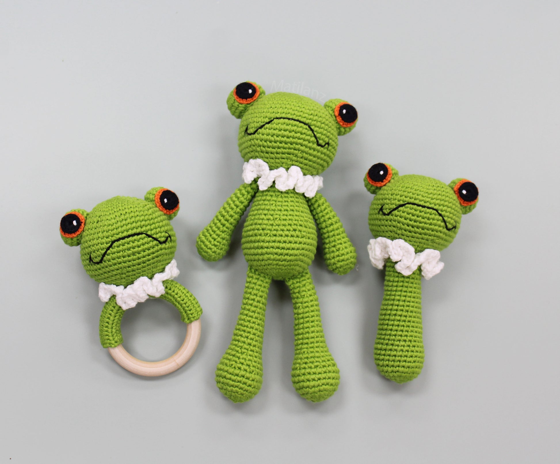 Handmade green crochet frog toy set with textured eyes and white ruffled collars, including a ring for sensory play.
