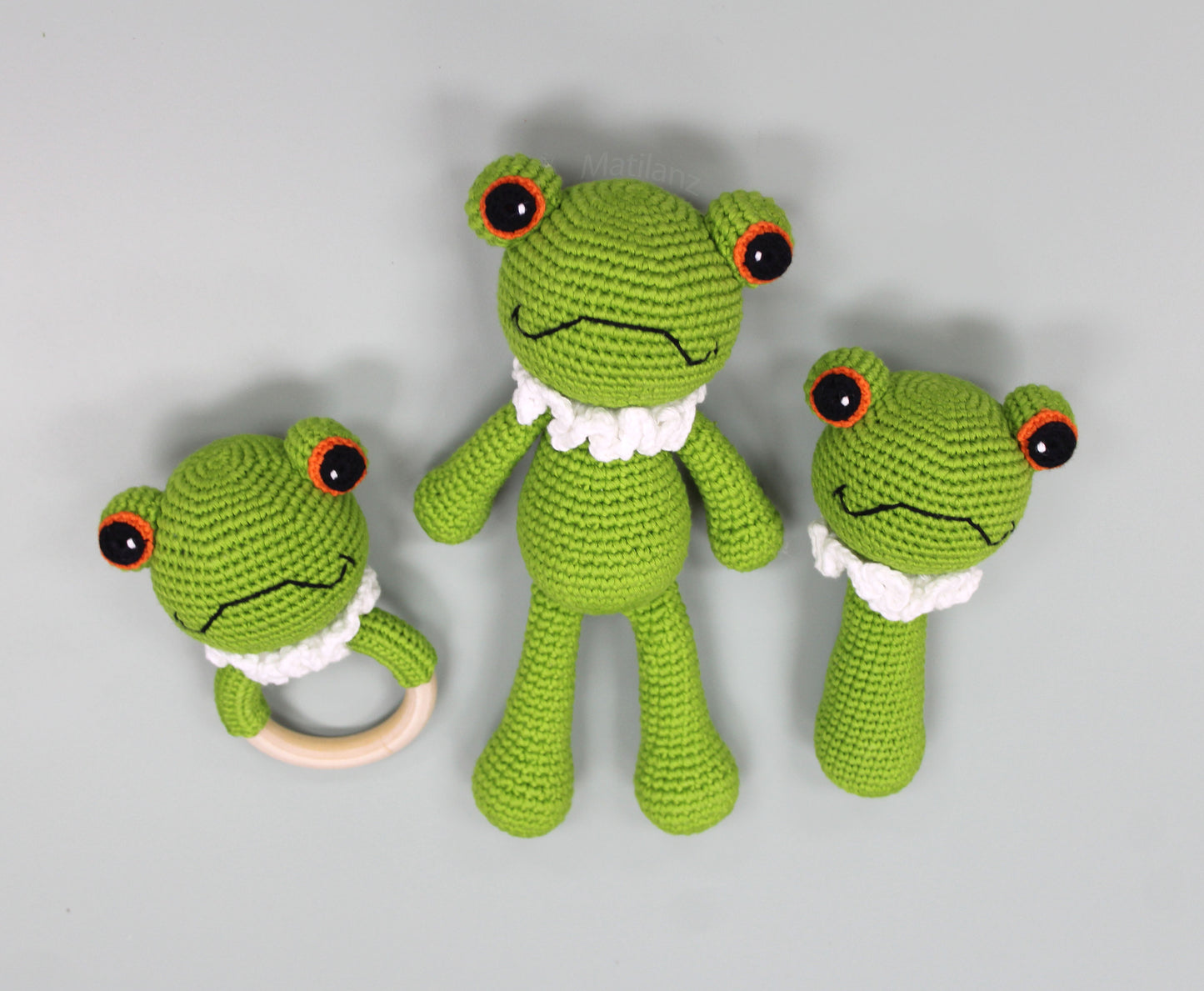 Handmade green crochet frog toy set with white ruffled collars and large black eyes, including a rattle.