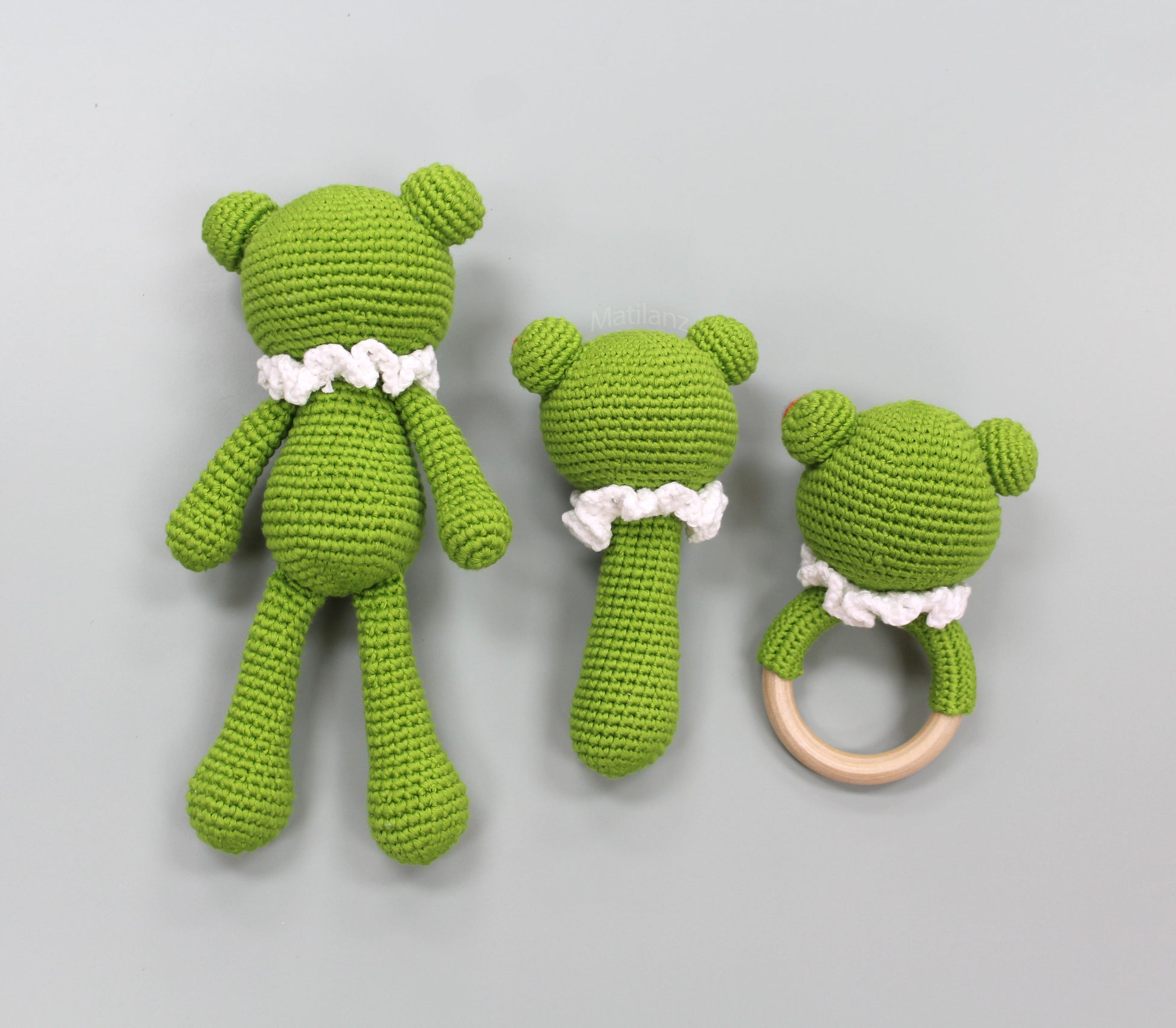 A handmade green crochet frog baby toy set, featuring a three-piece sensory collection with white ruffled accents and a wooden ring.