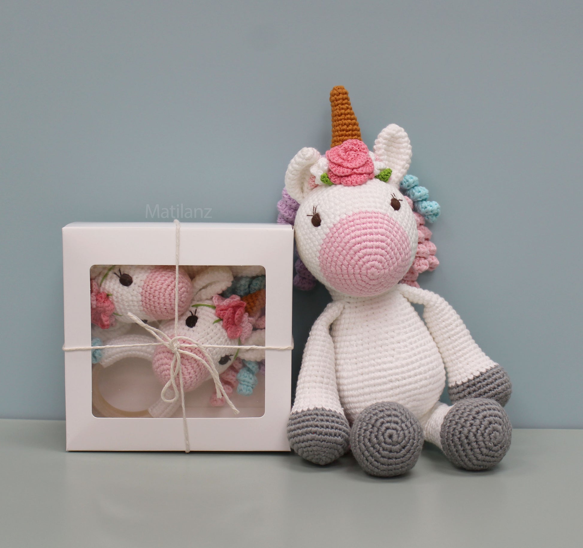 Handmade crochet unicorn baby toy with colorful mane, pink flower, and soft white body.