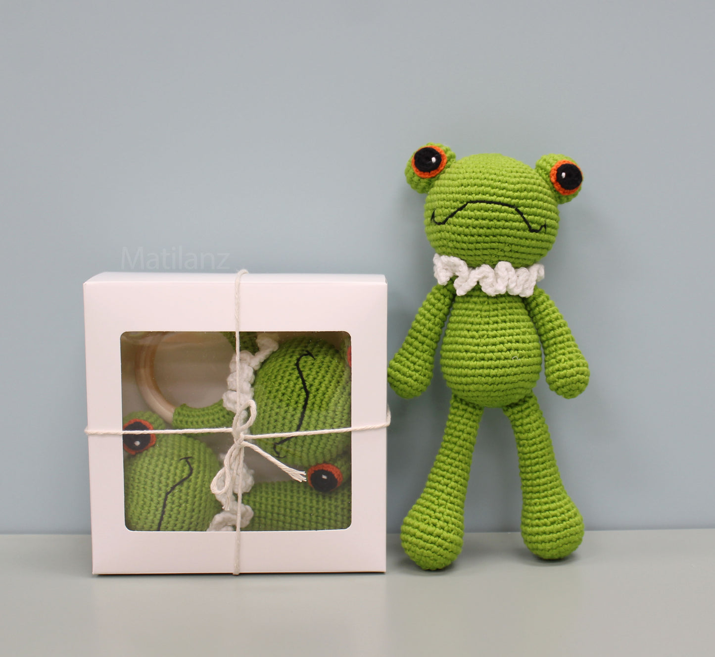 Handmade green crochet frog sensory toy set with white collar and red eyes, packed in a white gift box.