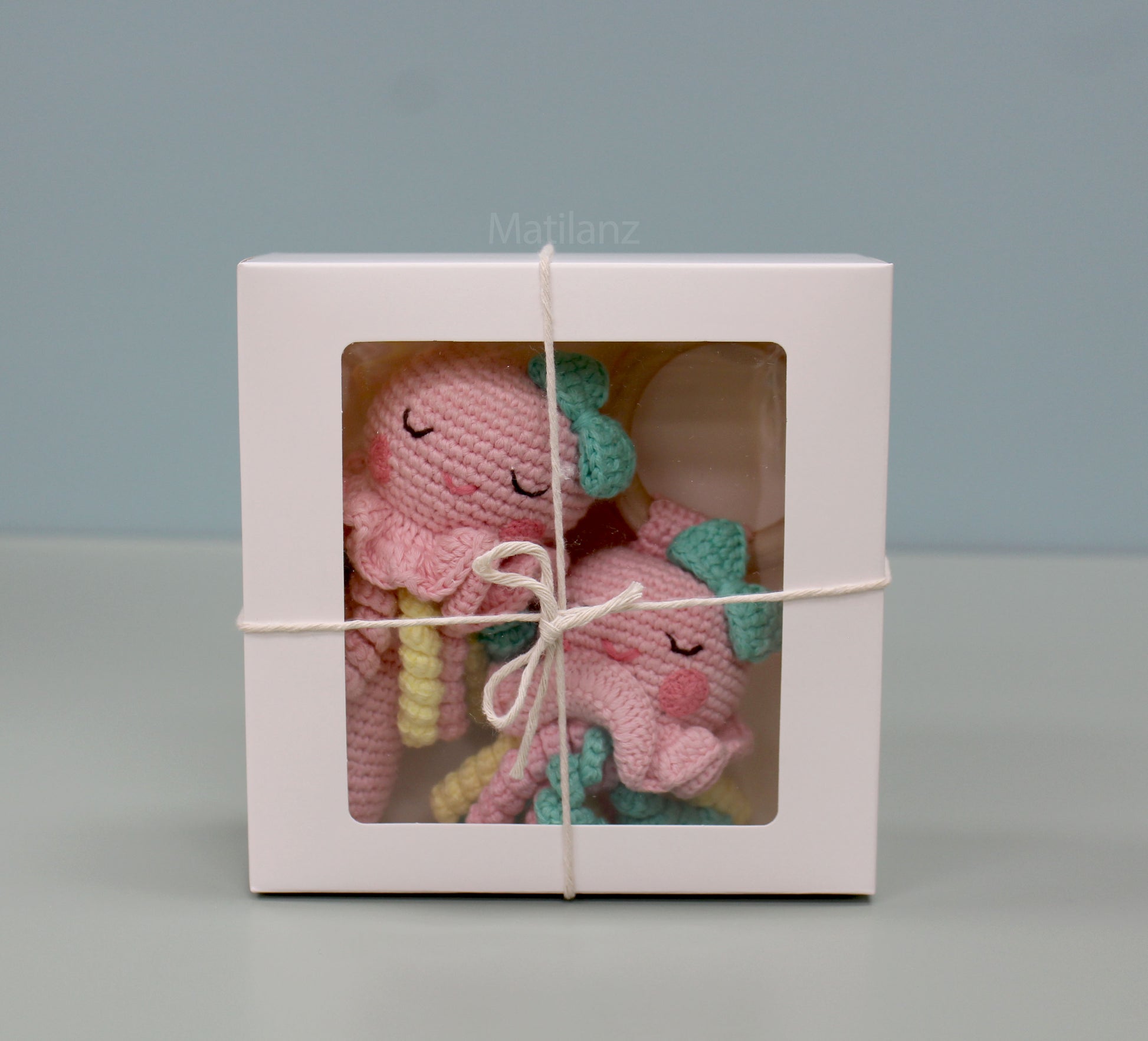 Pink handmade crochet jellyfish soft toys with yellow antennae and green bows, nestled in a white gift box.