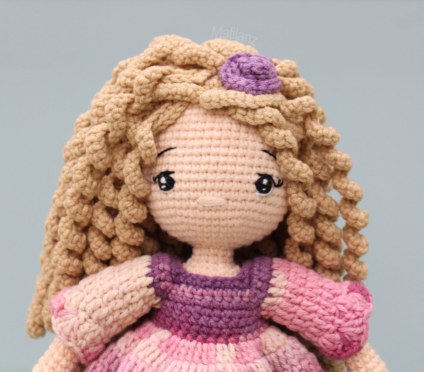 Handmade crochet doll with blonde curls, a purple accent, and a pink and purple dress.
