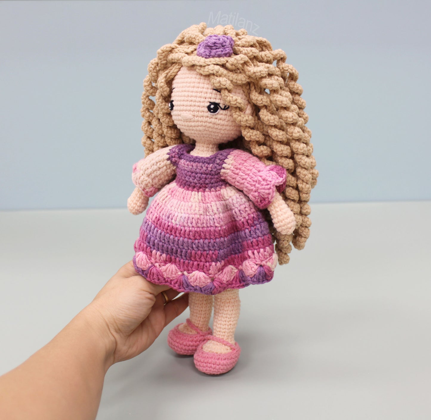 Handmade crocheted doll with long curly hair, wearing a pink and purple striped dress and matching shoes.