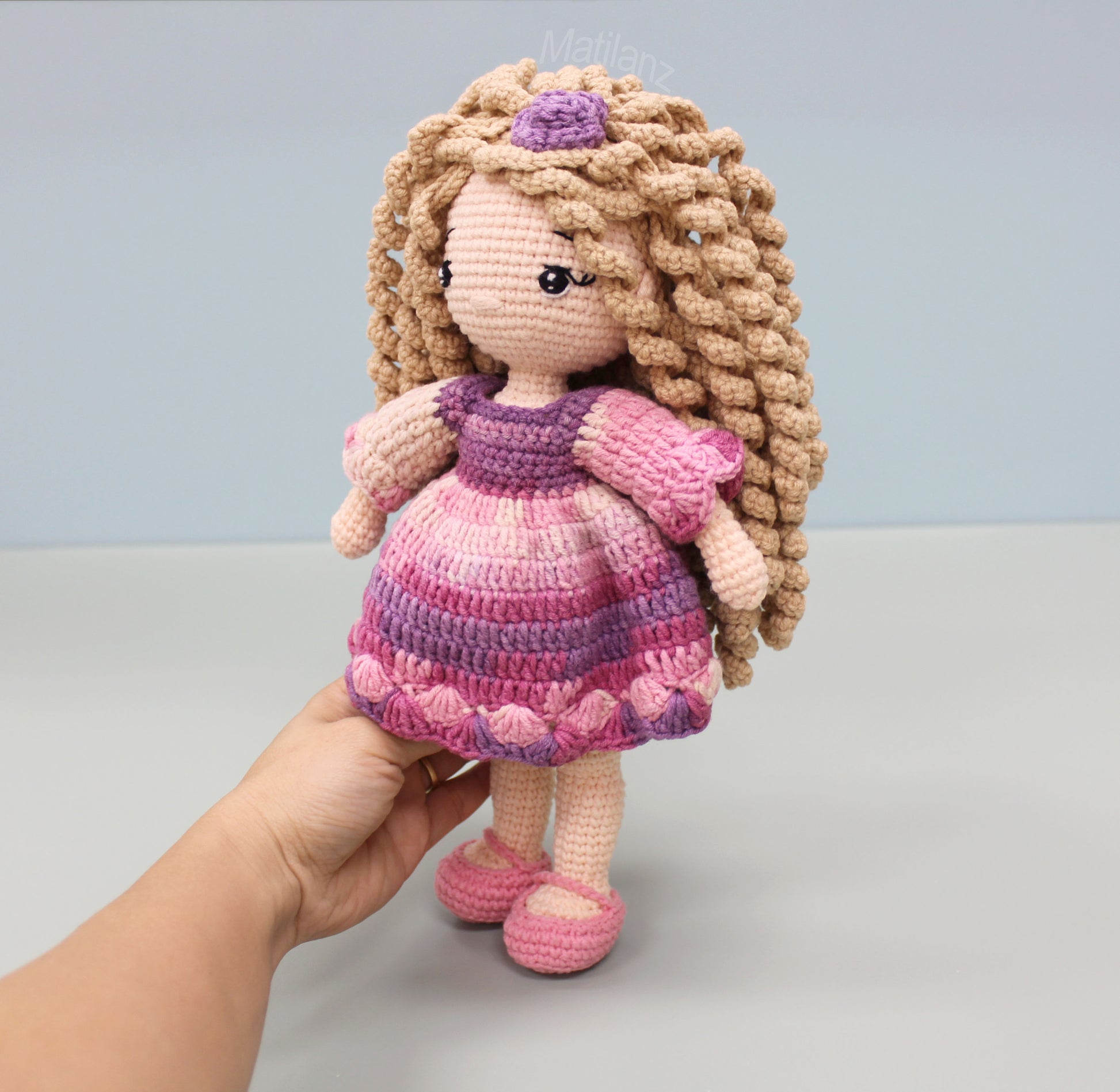 Handmade crocheted doll with long curly hair, wearing a pink and purple striped dress and matching shoes.