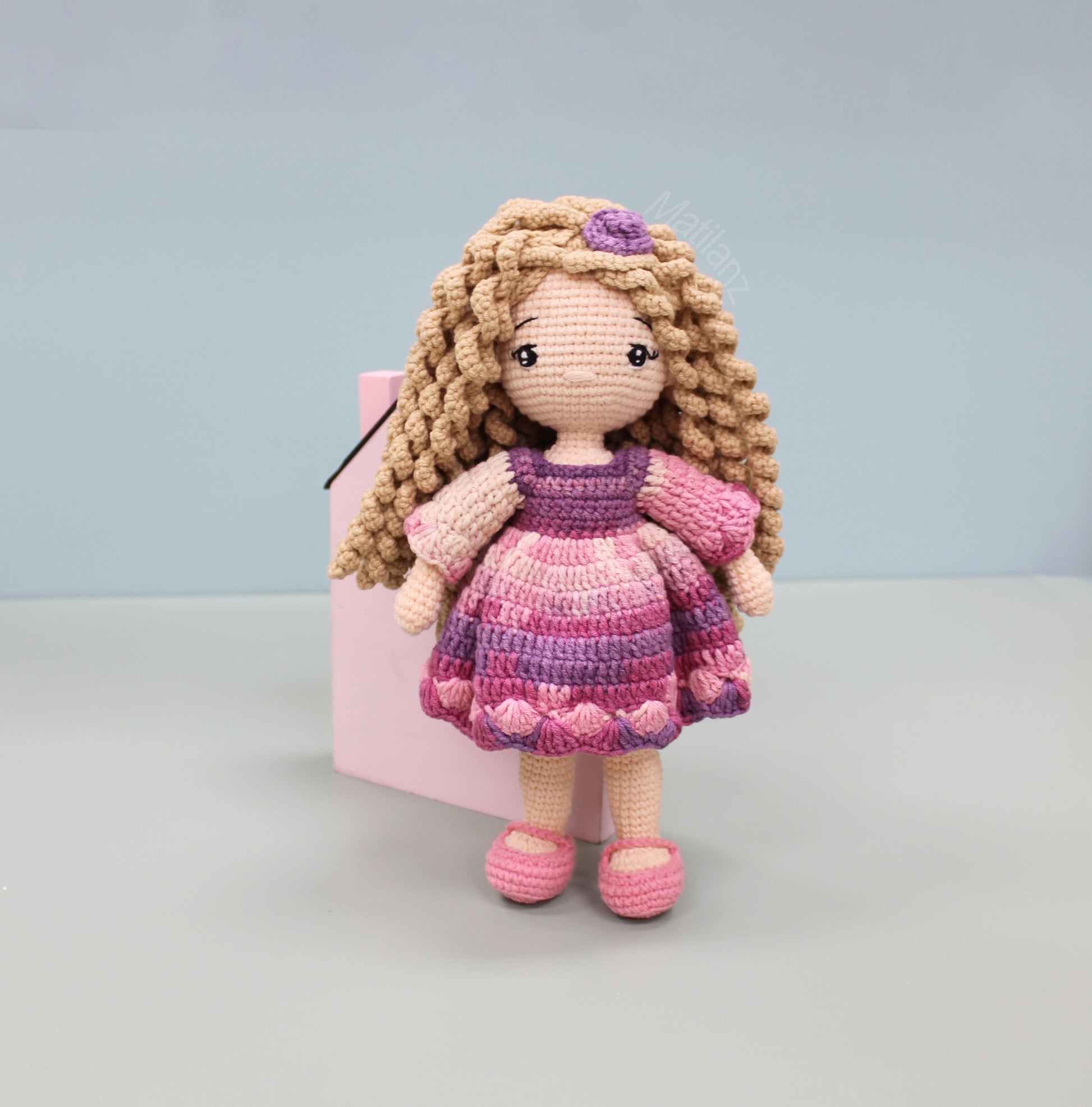 Handmade crochet doll with curly blonde hair, wearing a pink and purple dress and matching shoes.