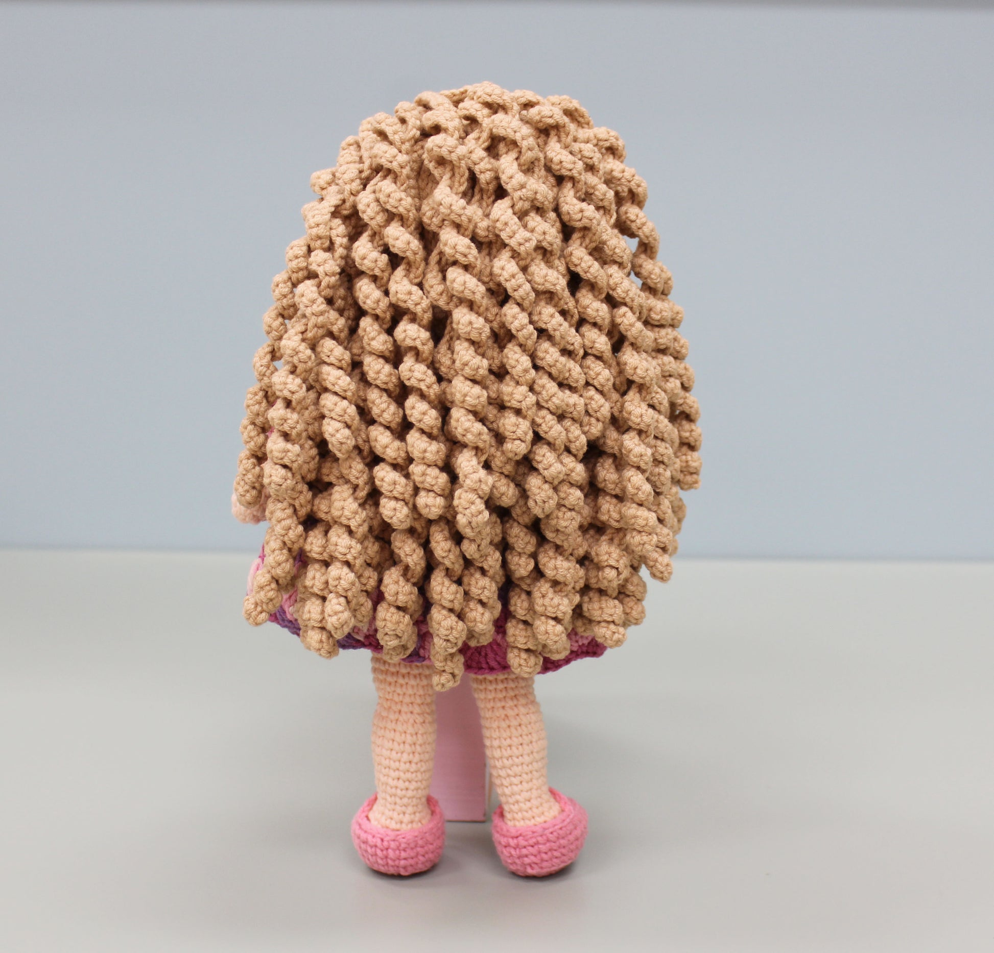 Handmade crochet doll with textured hair, pink and purple dress, and pink shoes.