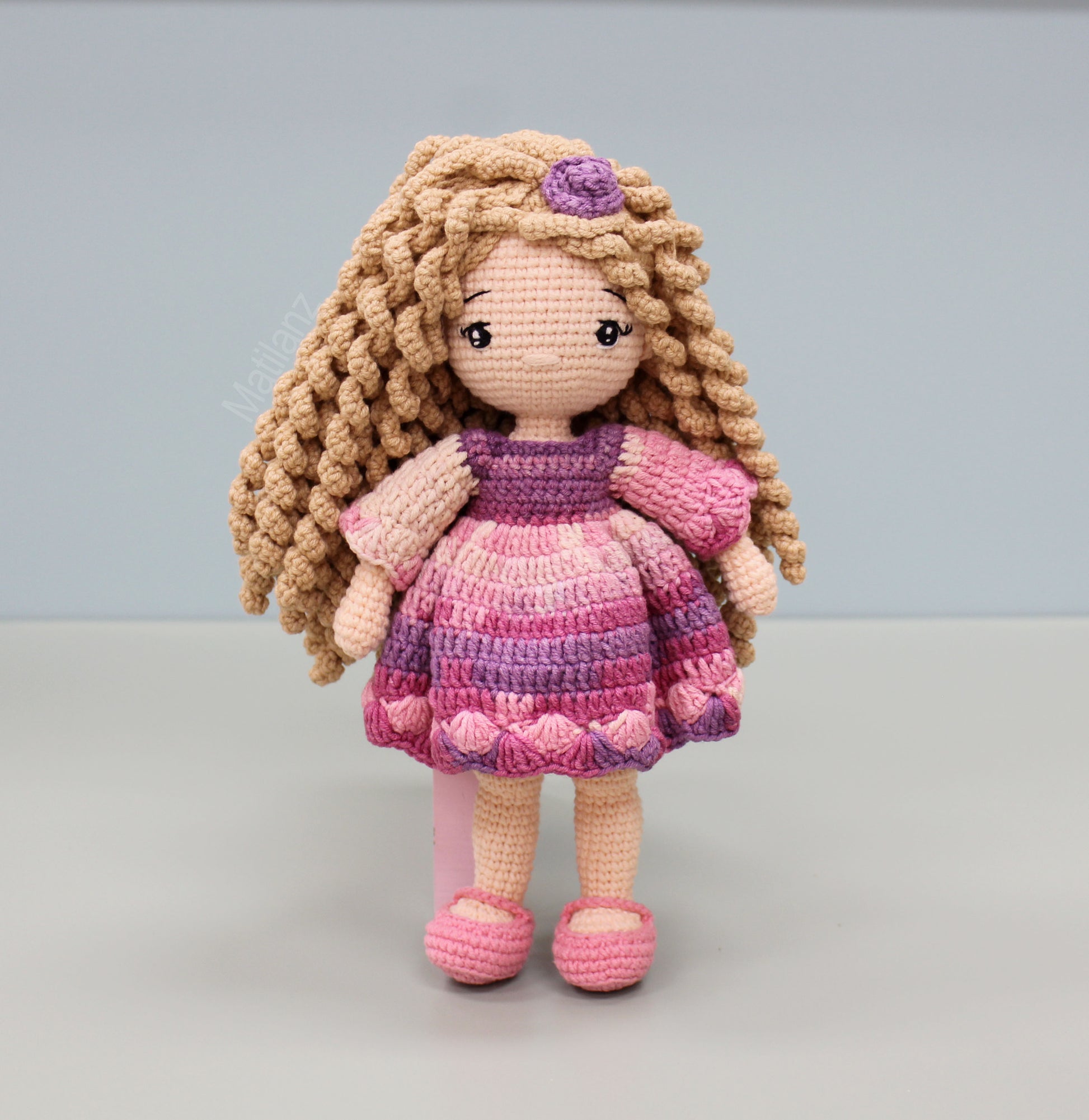 Handmade crochet doll with long blonde hair, wearing a soft pink and purple dress and shoes.