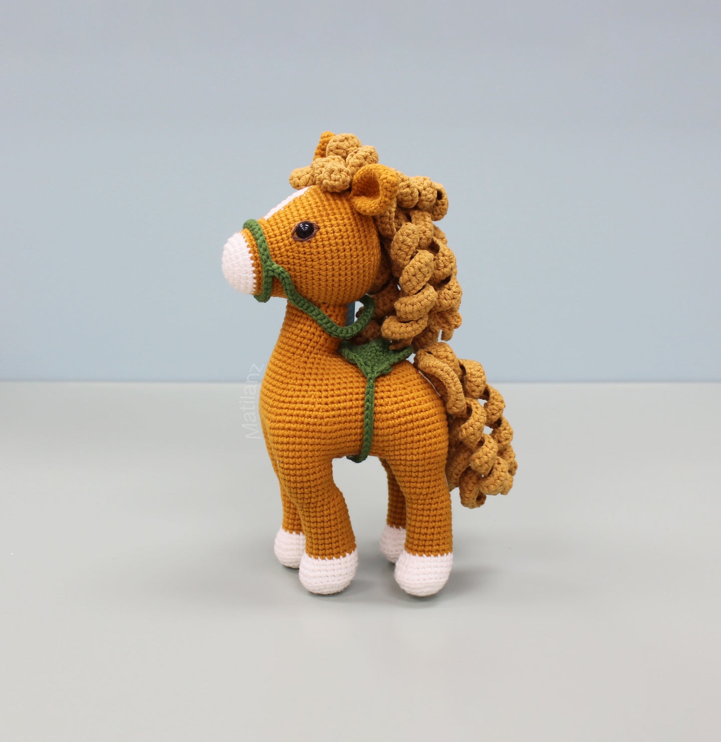 Handmade 10-inch crochet horse in copper with a green harness and curly mane.