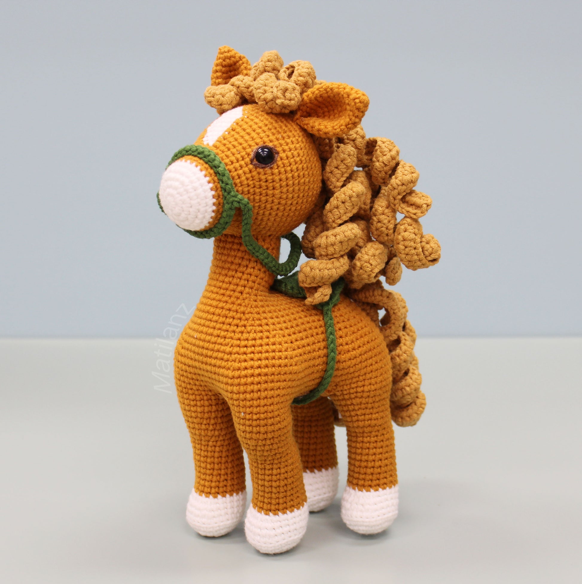 Handmade crochet horse in copper hue, featuring detailed mane, tail, and green bridle straps.