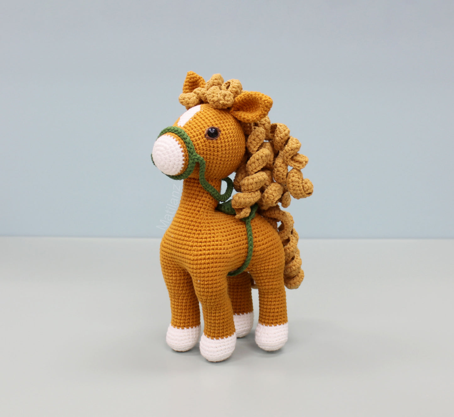 Handmade 10" crochet horse with golden-brown body, white hooves, and green bridle.