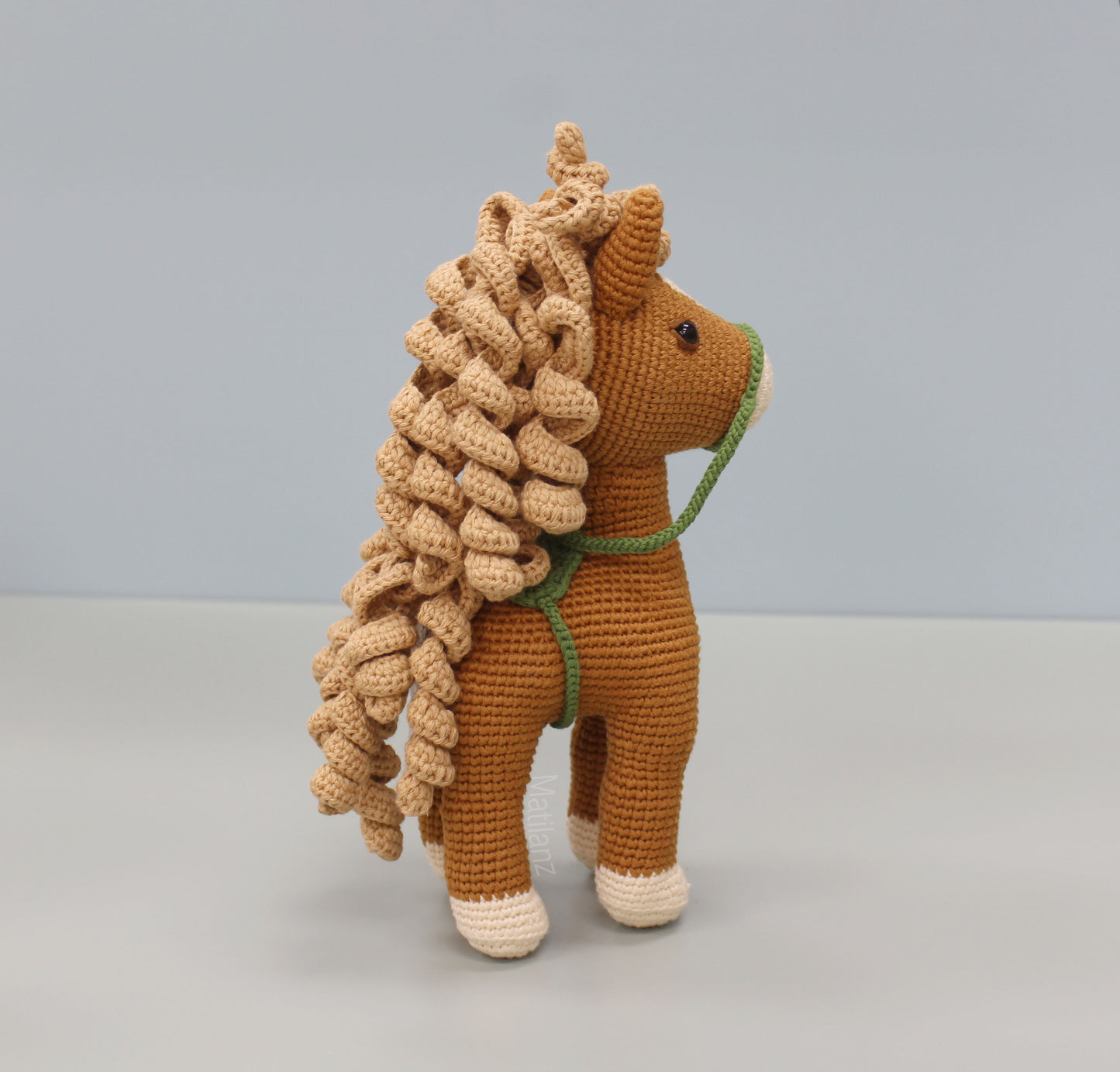 Handmade crochet horse soft toy in copper with cream-colored hooves and a green halter.