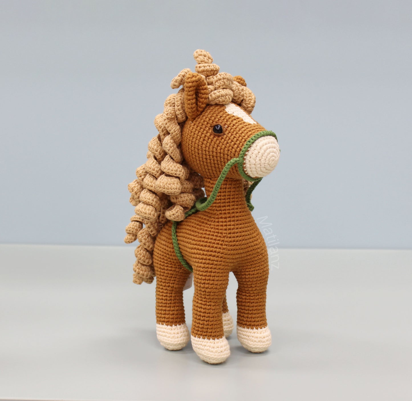 Handmade crochet horse soft toy, made of cotton, featuring brown and white colors with a green bridle.