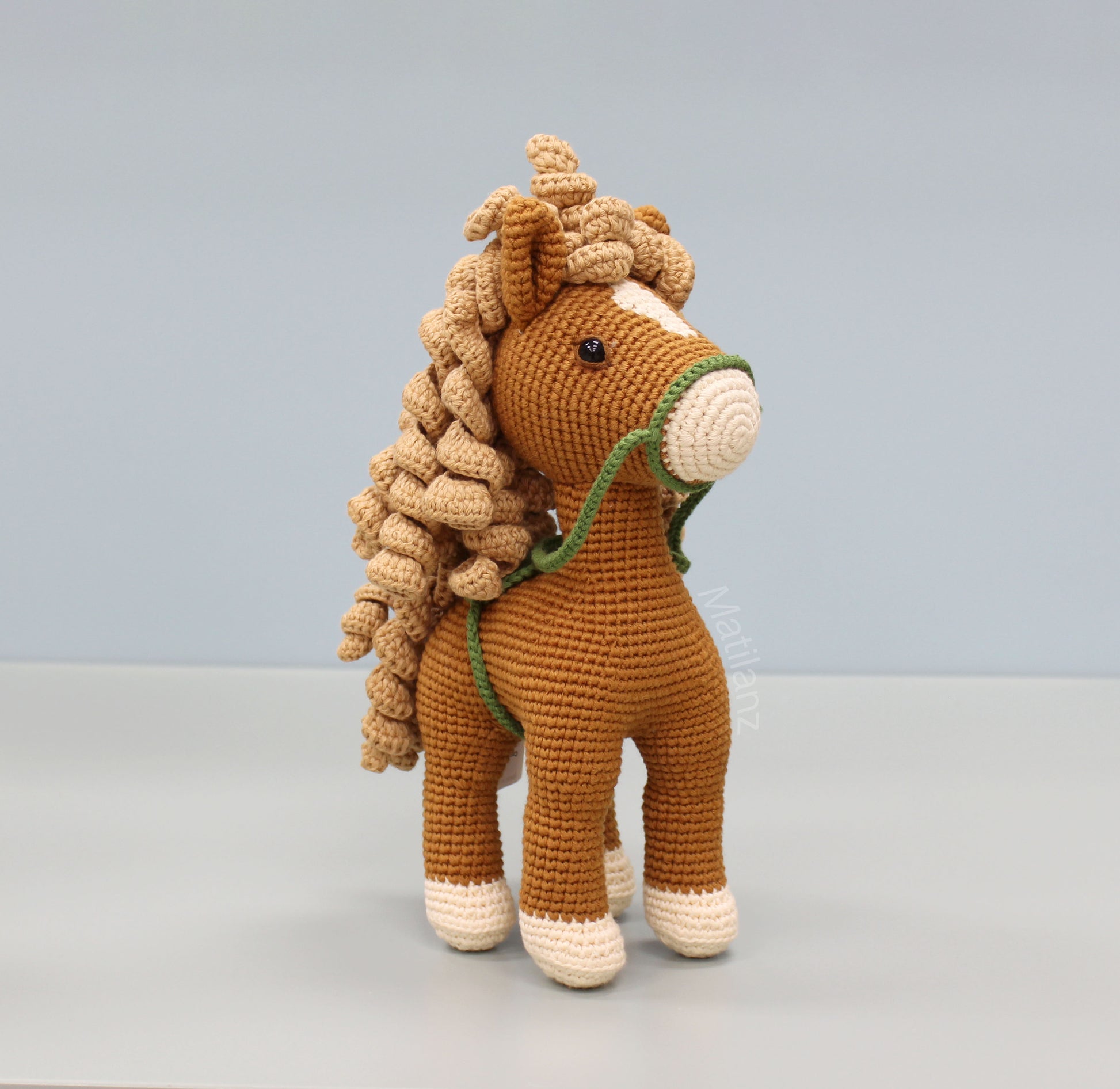 Handmade crochet horse soft toy, made of cotton, featuring brown and white colors with a green bridle.