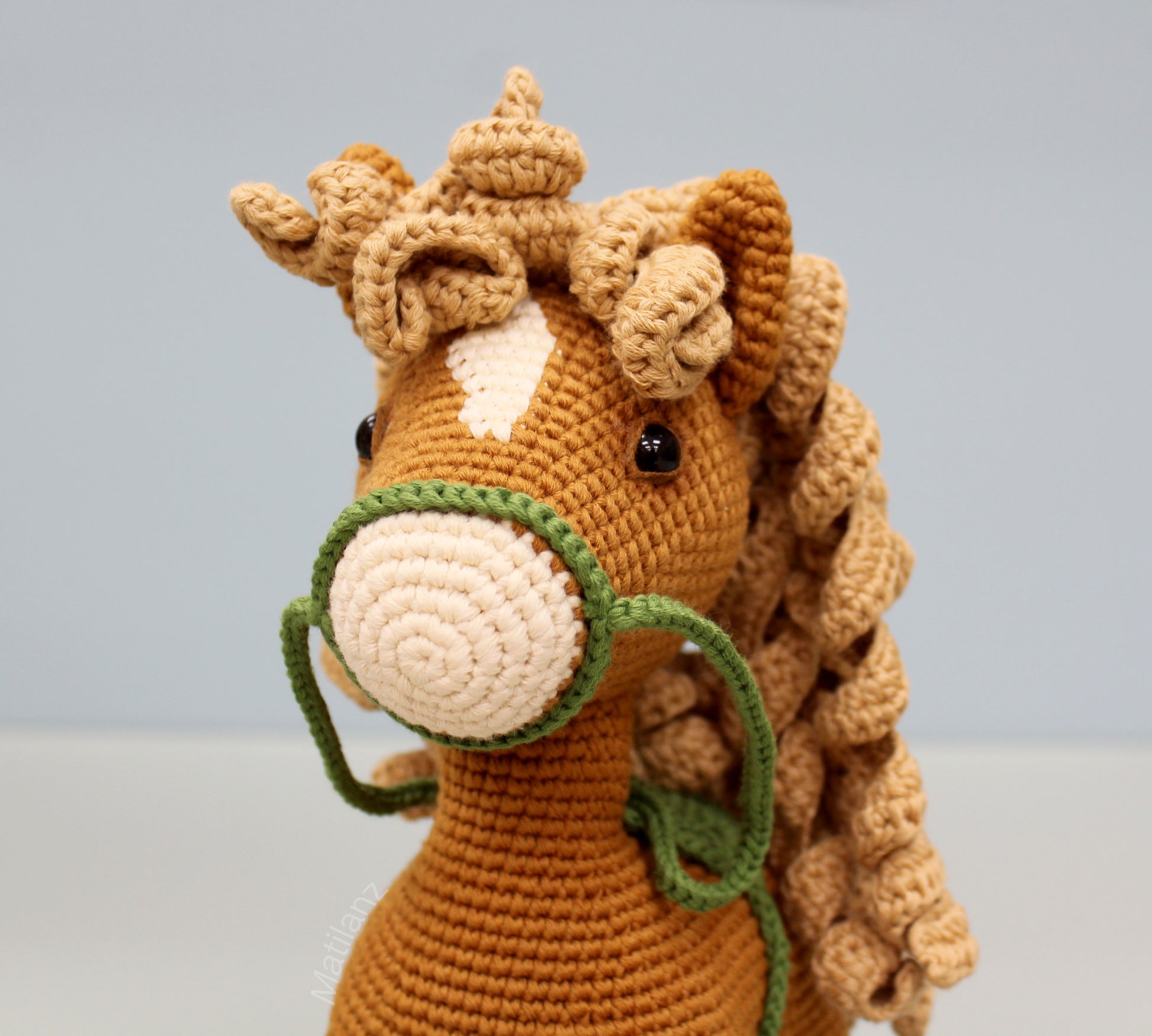 Handmade copper-colored crochet horse with a cream muzzle, green reins, and fluffy yarn mane.