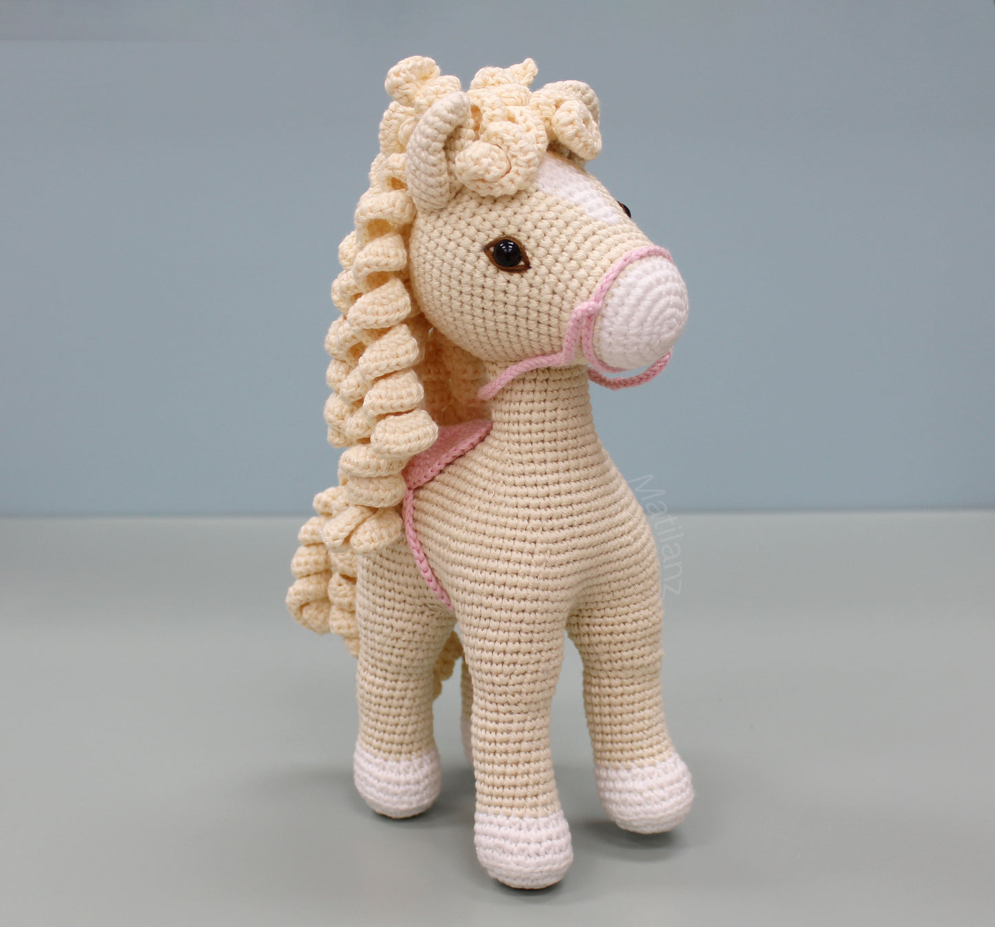 A handmade white crochet horse soft toy with a textured mane and pink bridle.