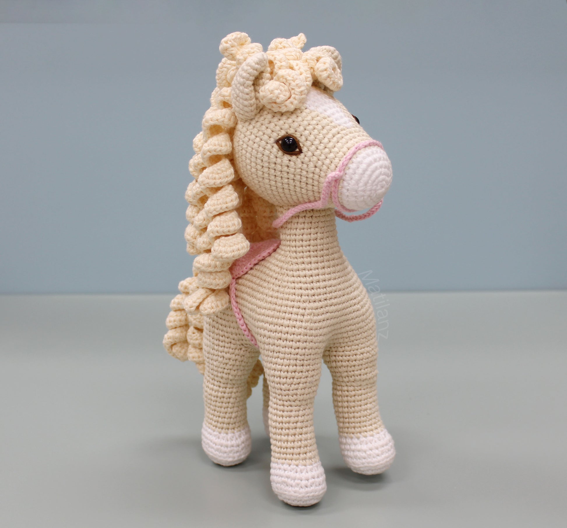 A handmade white crochet horse soft toy with a textured mane and pink bridle.