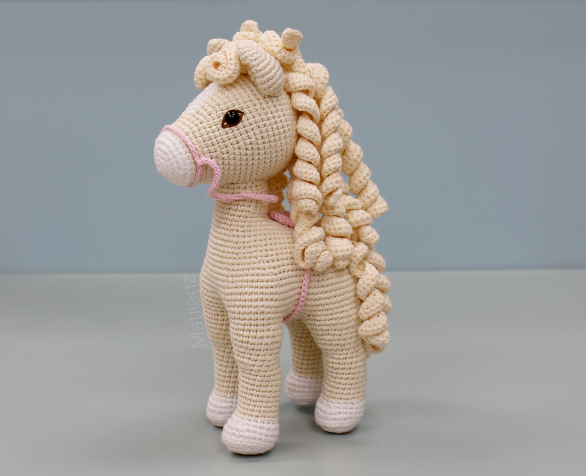 Handmade white cotton crochet horse soft toy with pink details and braided mane and tail.